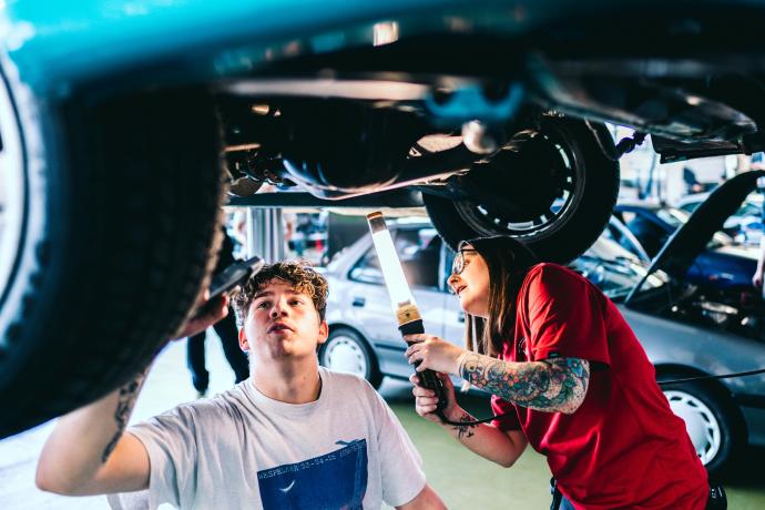 Studenten autotechnologie bekijken de onderkant van een auto.